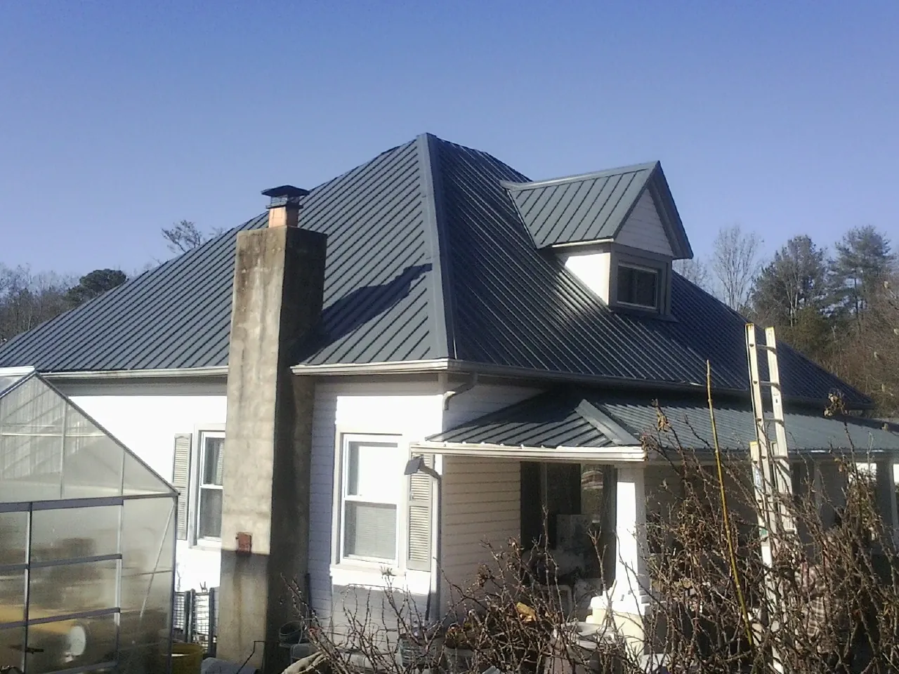 Dark blue standing seam metal roof on a white farmhouse with dormer — Slate & Tile Roof Repair by Roofing Brothers in Plevna