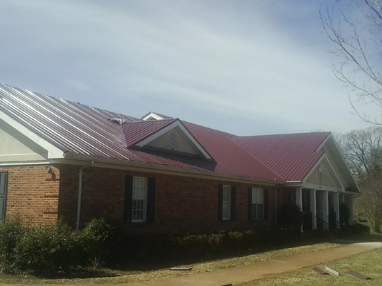 Red metal roof with gabled entries on a long brick building, from a Hail Damage Roof Repair job in Plevna