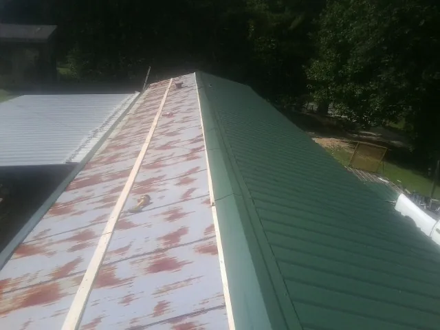 Old rusted panels beside newly installed green metal roofing — Wind Damage Roof Repair by Roofing Brothers in Plevna
