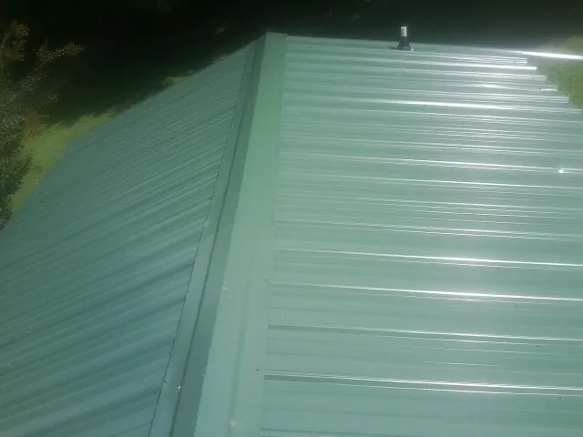 New green metal panels meeting at the ridge of a roof — Flat Roof Repair work by our crew in Plevna