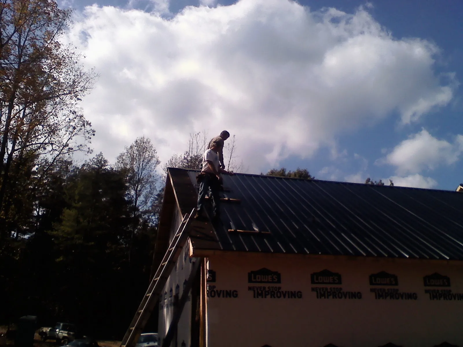 Roofer fastening dark metal panels high against a cloudy sky, from a Roof Inspection job in Plevna