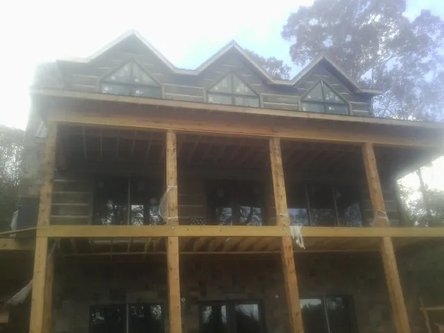 Dormers and porch framing on a large log home under construction — Roof Coating work by our crew in Plevna