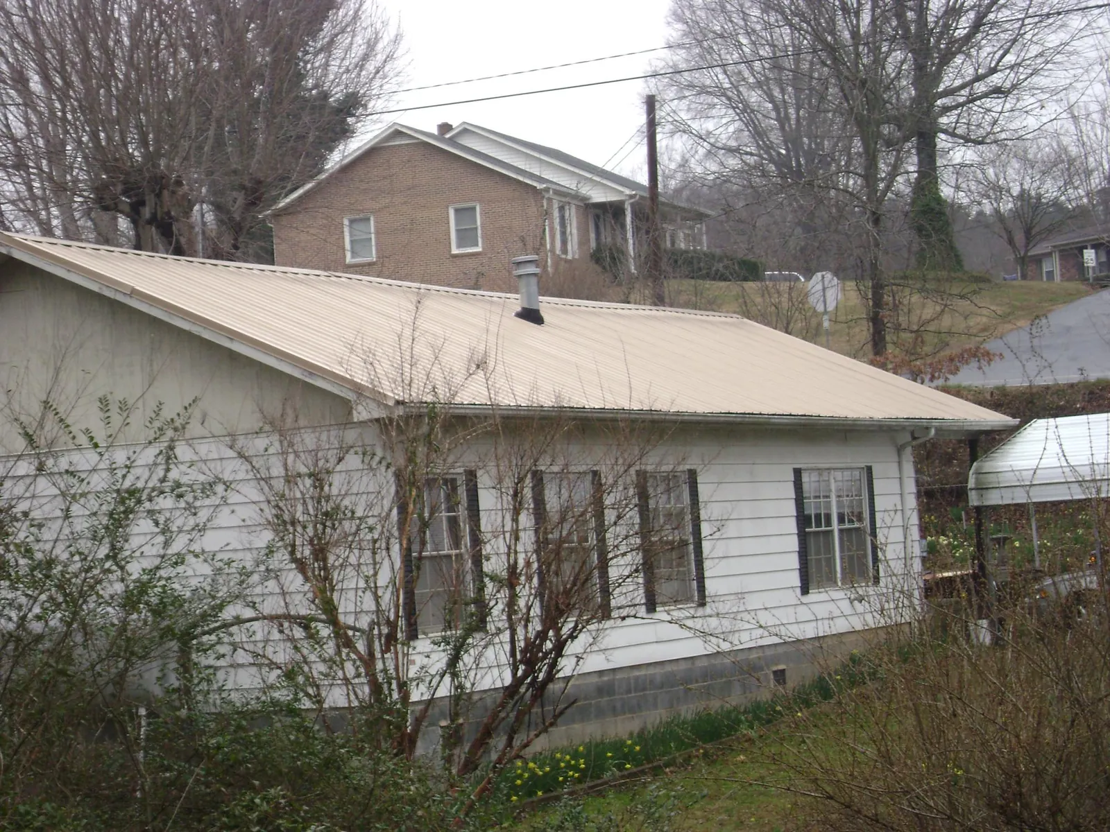 Tan metal roof on a white sided house set into a hillside — Commercial Roofing by Roofing Brothers in Plevna