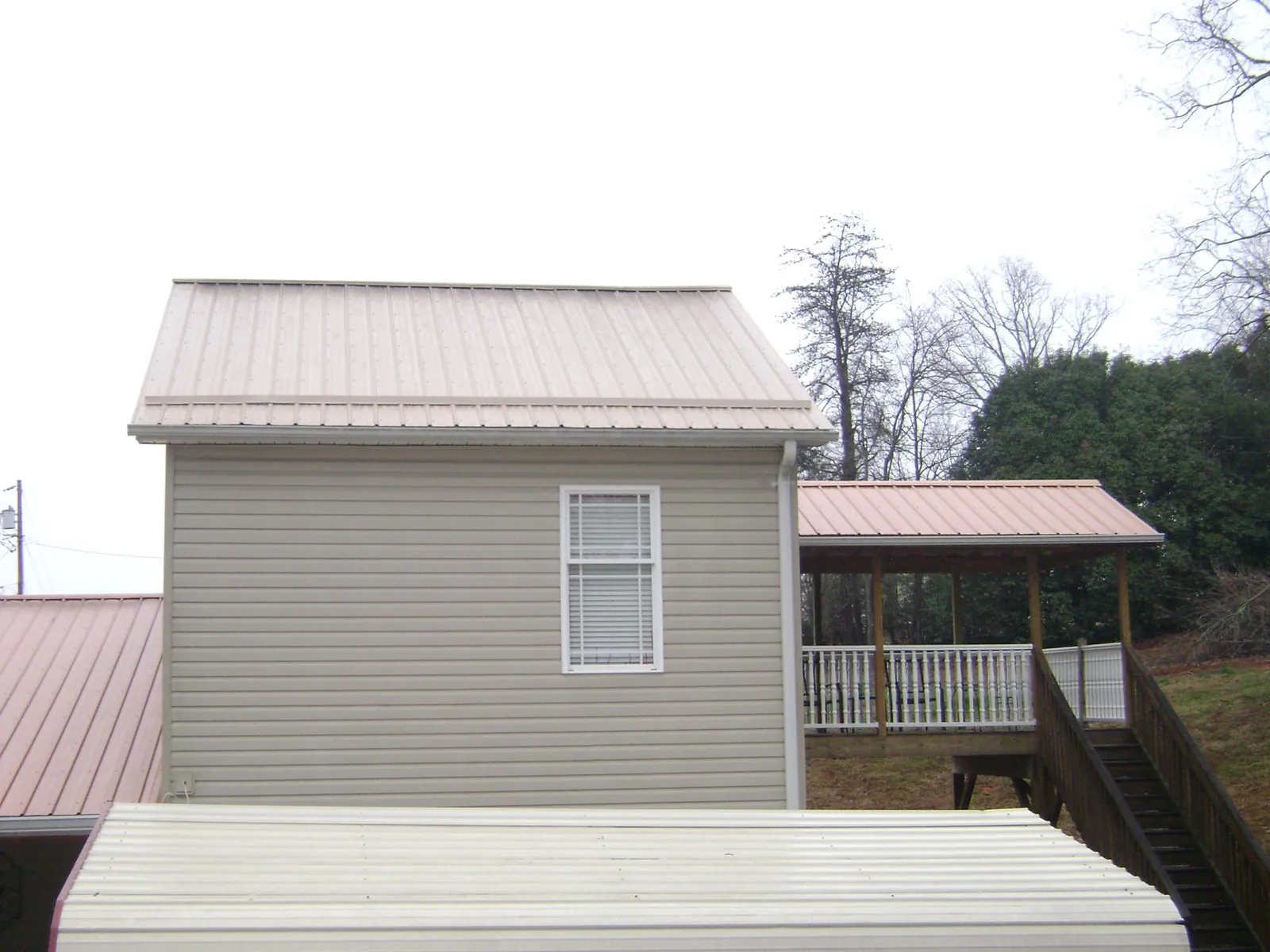 Tan metal roofs on a two story addition and attached porch, from a Roof Replacement job in Plevna